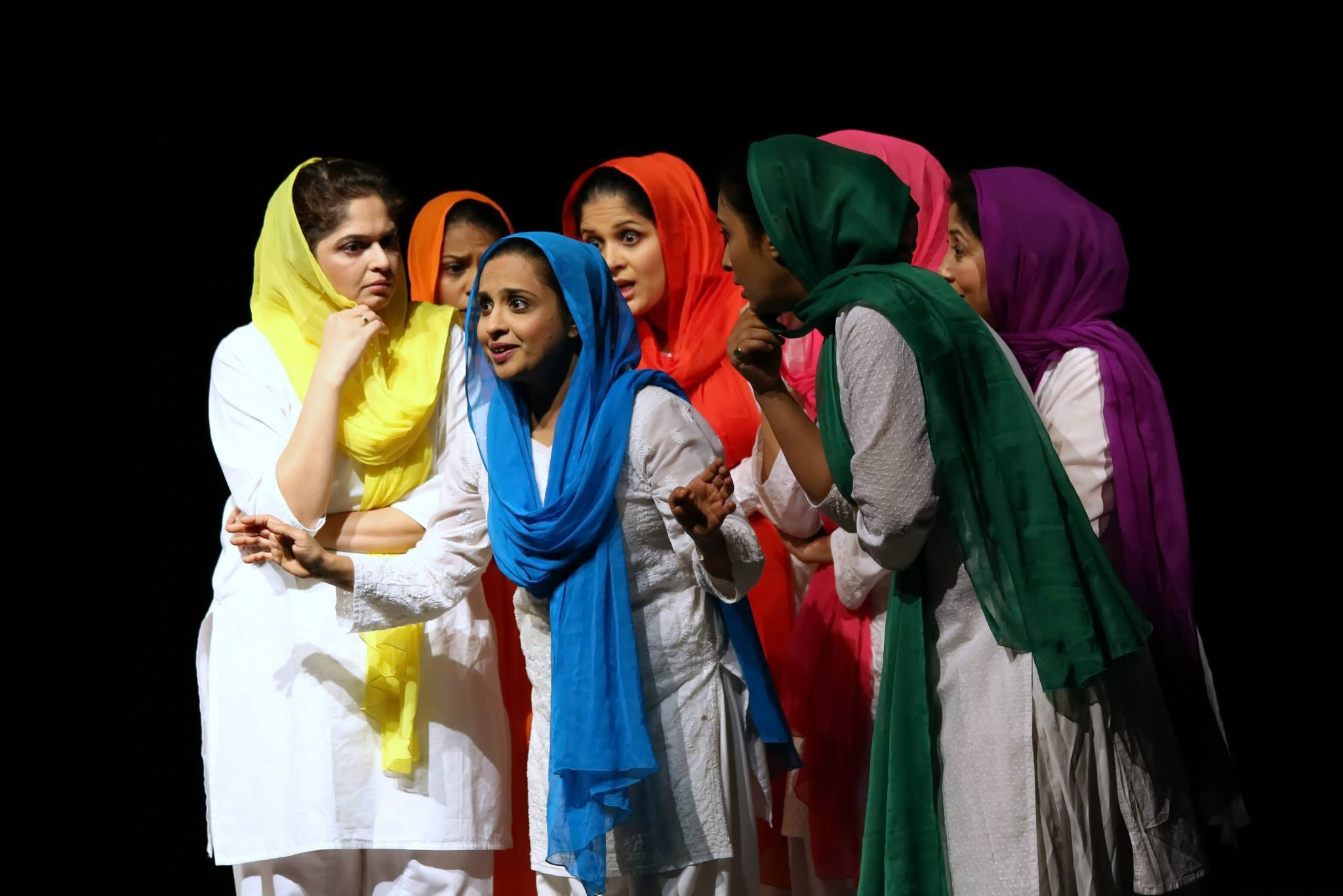 An ensemble of women performing on stage in white costumes and brightly coloured scarves.